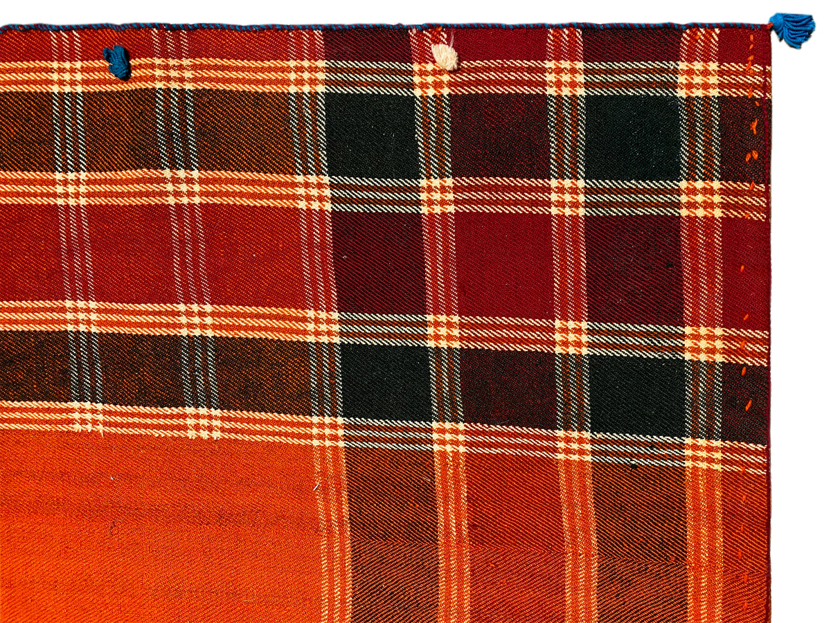 Detalhe do tapete Jajim: padrão axadrezado vermelho-alaranjado intenso, com áreas pretas e linhas brancas