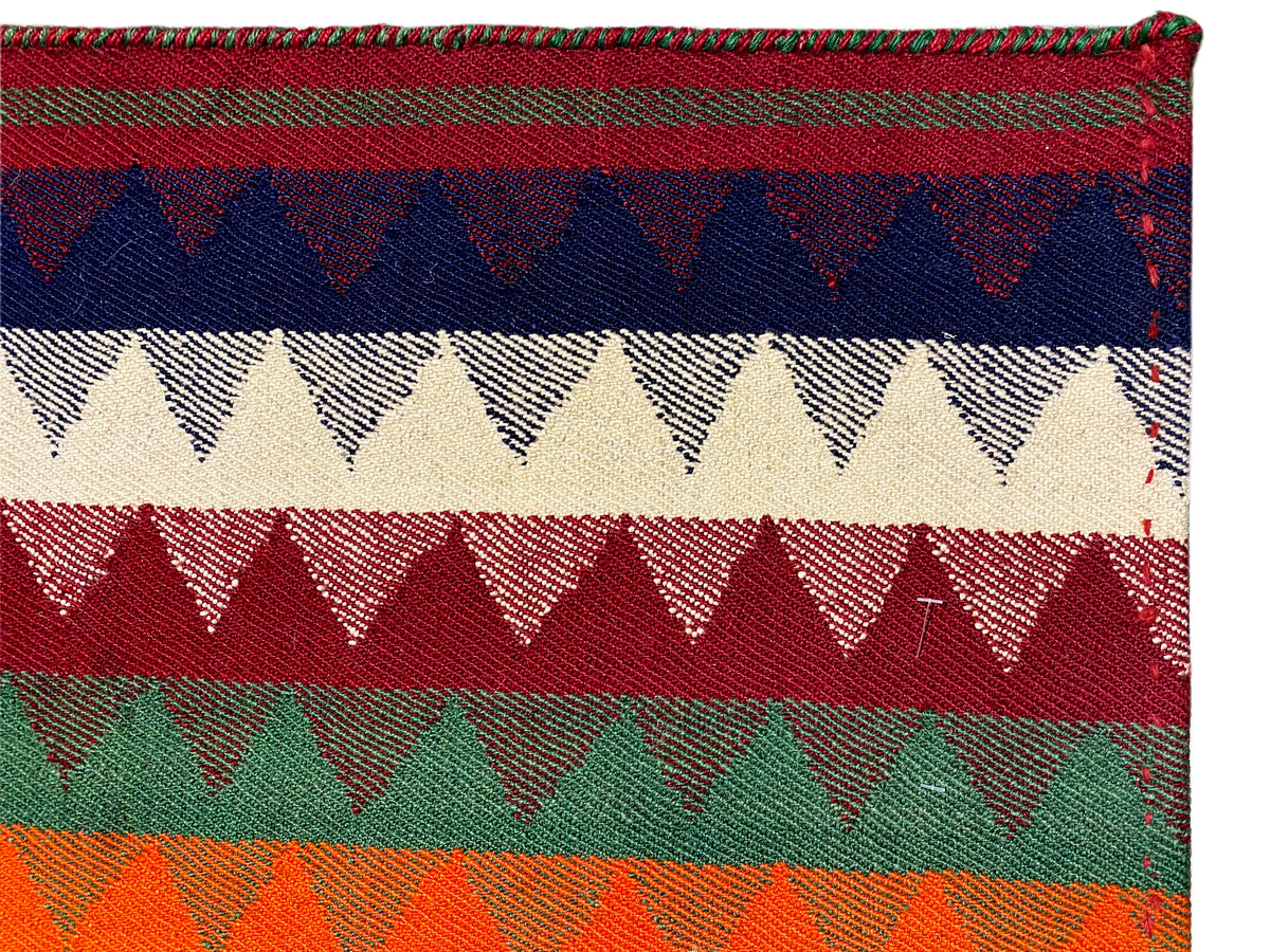 Grande plano de um tapete Jajim: faixas coloridas com remates em ziguezague e textura tecida