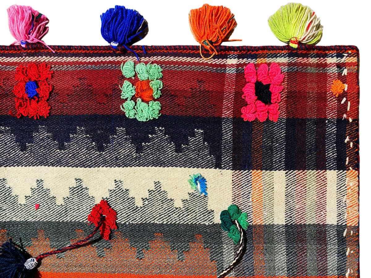 Grande plano: tapete Jajim com padrão aos quadrados, motivos florais e borlas multicolores