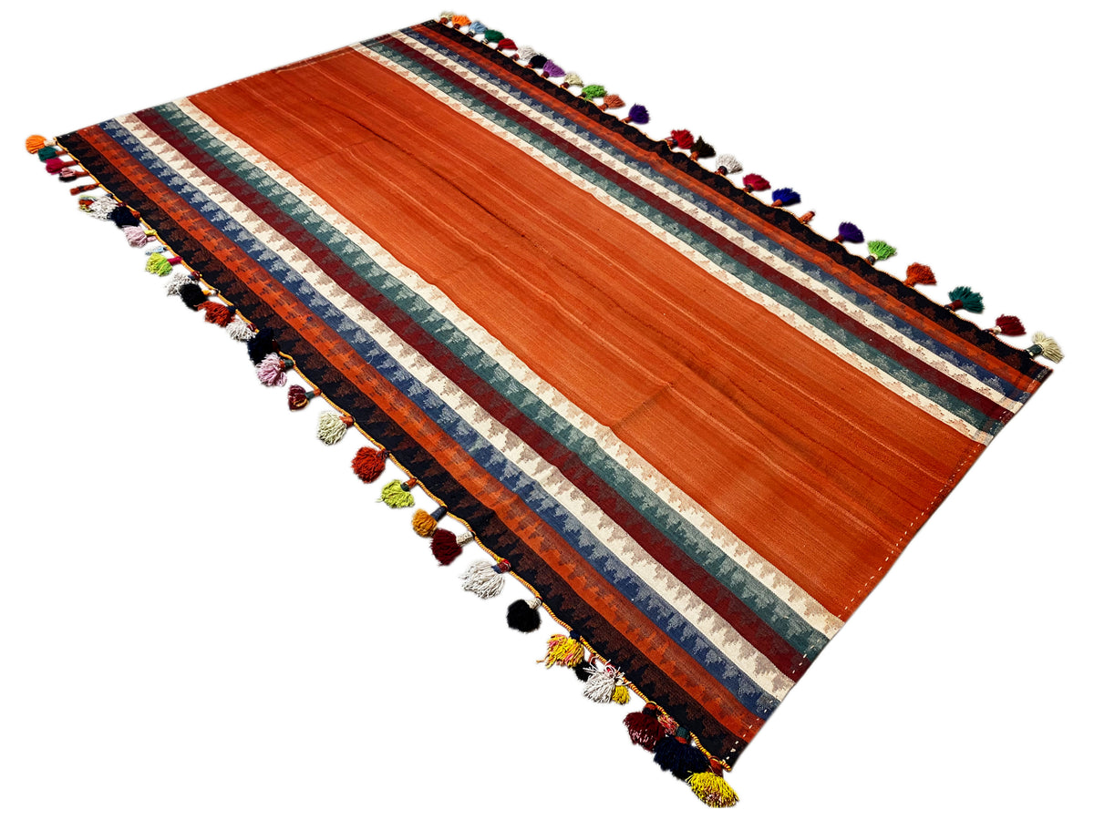Tapete Jajim estendido na diagonal: terracota, borda às riscas, franjas de várias cores