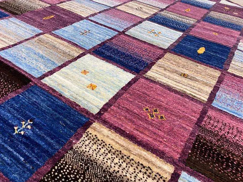 Vista aproximada de um tapete Gabbeh: quadrados de patchwork, áreas azuis e cor de vinho com padrões