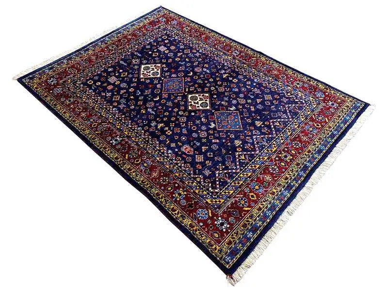 Tapete oriental azul-escuro na diagonal, com moldura vermelha e padrões de medalhões