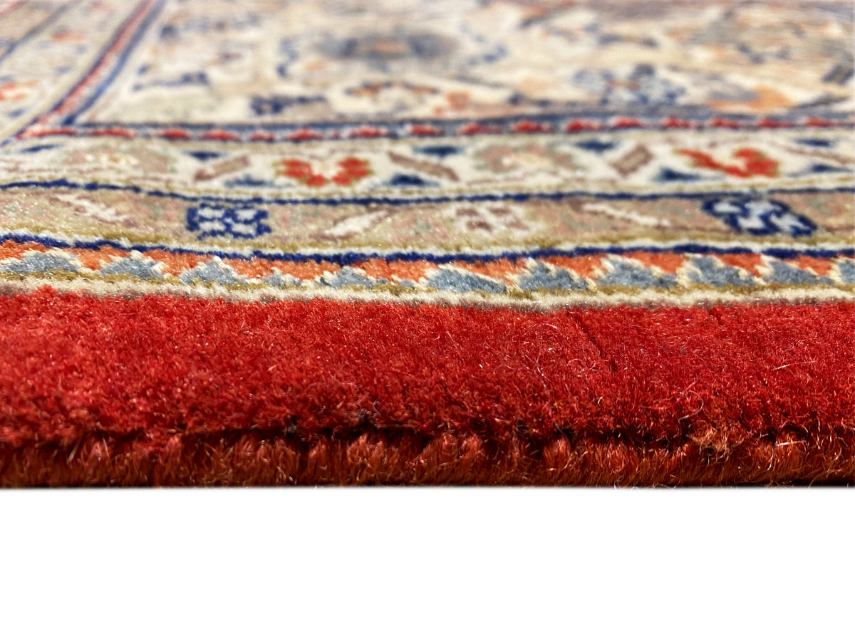 Margem de tapete com franjas e pelo de tom castanho-avermelhado; por baixo, uma borda decorativa multicolorida