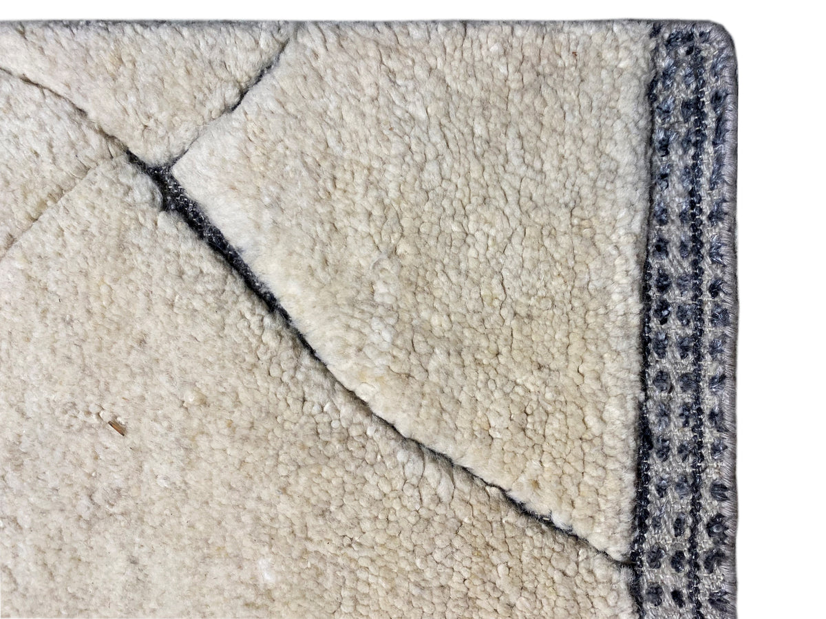 Plano de pormenor da borda do tapete: pelo cor de creme com debrum decorativo azul