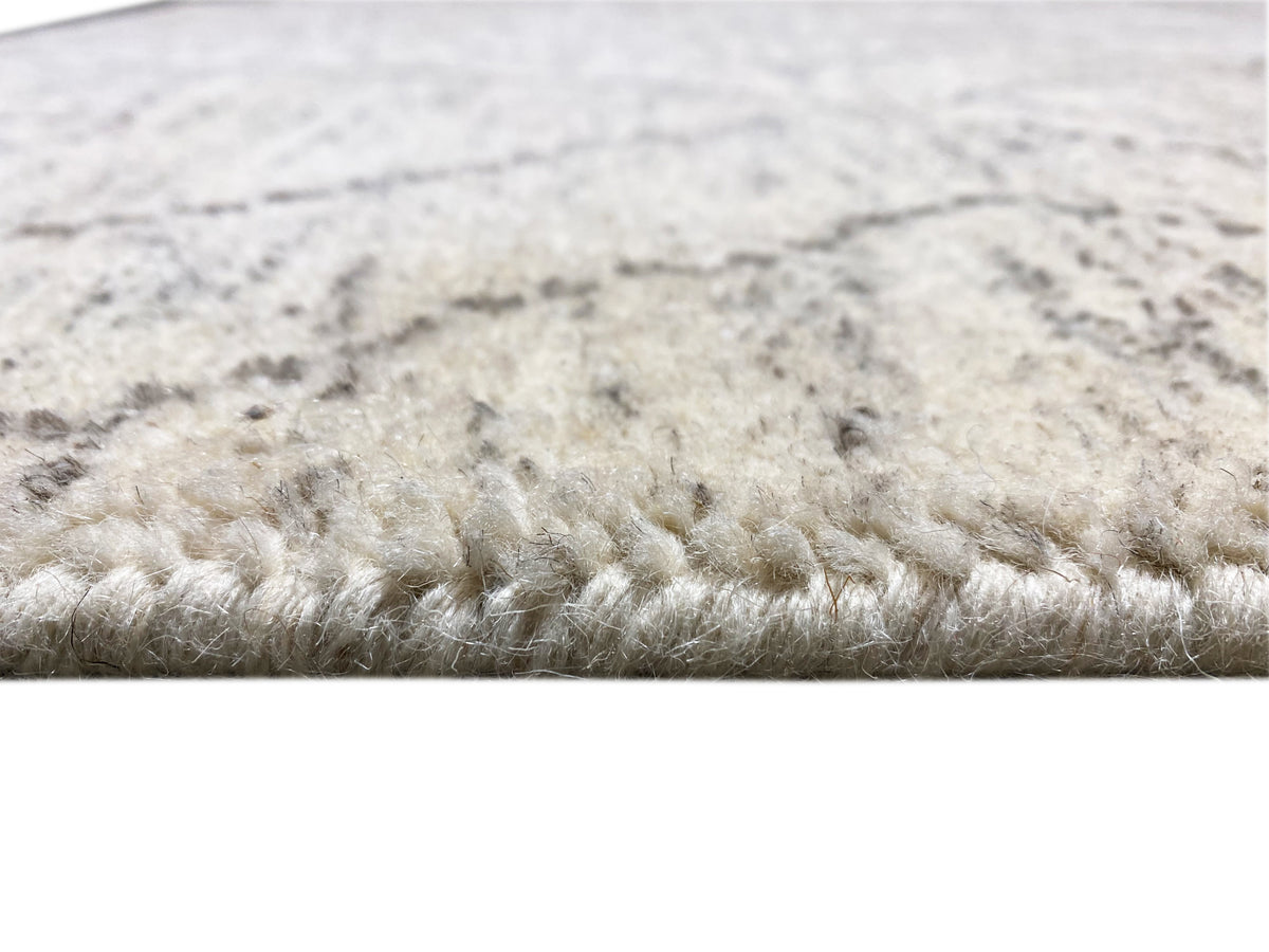 Grande plano do rebordo do tapete: pelo denso em bege-claro com padrão marmoreado a cinzento