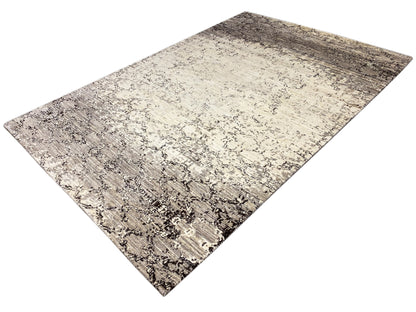Teppich mit hellem Beigegrund und dunkelgrauen Flecken sowie Ornamentlinien, diagonal