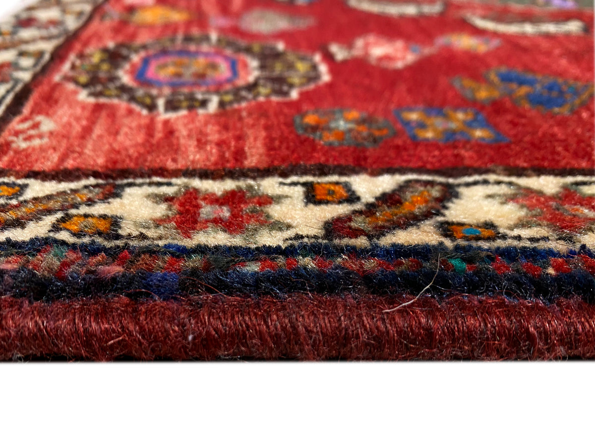 Pormenor do tapete Poshti 58x57 cm: pelo vermelho, rebordo com padrão colorido e franjas curtas
