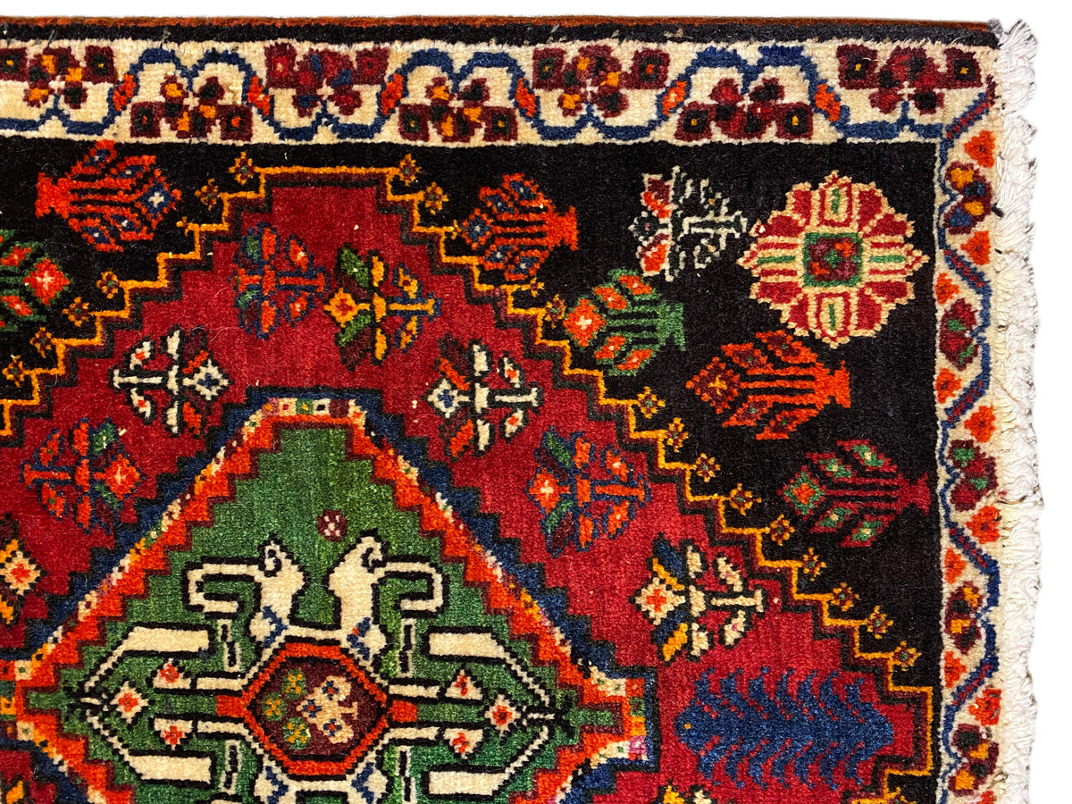 Vista aproximada de um tapete Poshti: tapete preto com medalhão verde e ornamentos coloridos