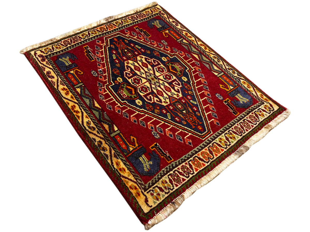 Tapete Poshti (59×61 cm) estendido na diagonal, padrão geométrico vermelho com franjas