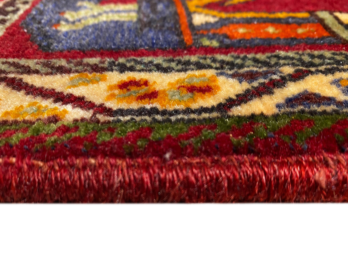 Tapete Poshti (59×61 cm) em grande plano: pelo vermelho e bordas coloridas com franjas