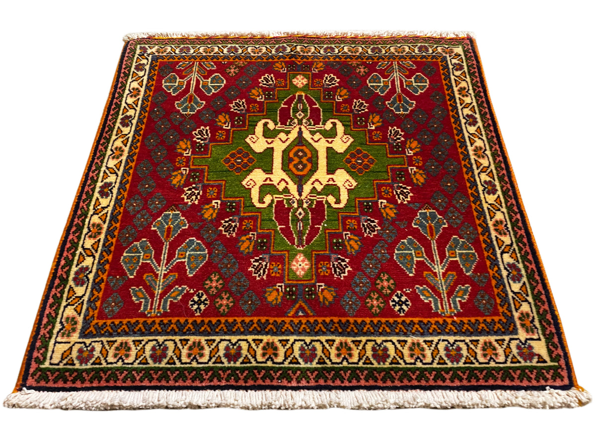 Tapete oriental com motivo central vermelho, detalhes verdes e borda bege, com franjas