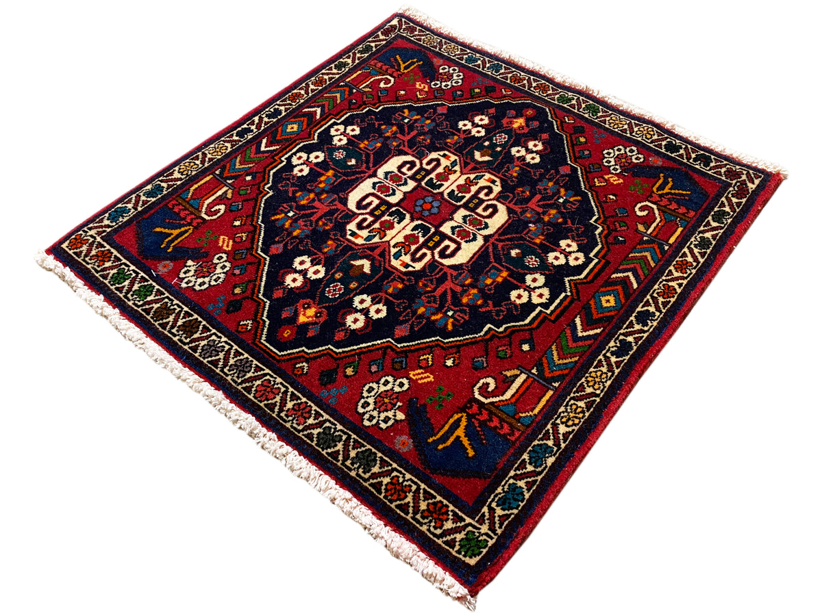 Tapete quadrado com orla decorativa, padrão vermelho e azul e centro creme.