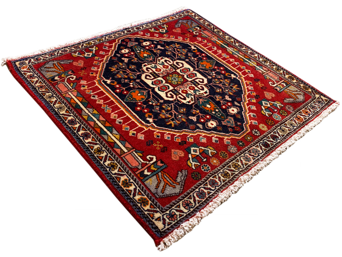 Tapete retangular com fundo vermelho e padrão ornamental azul, com franjas