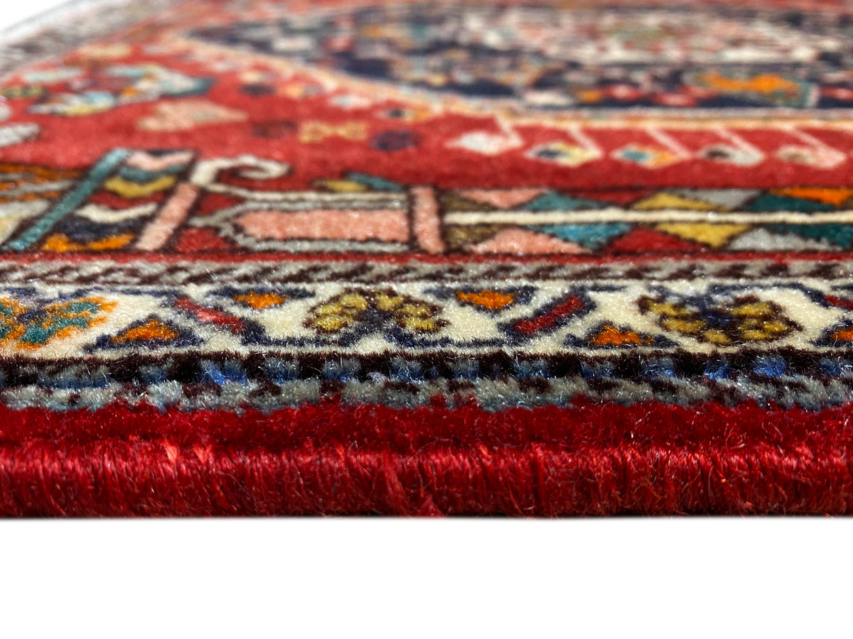 Detalhe do rebordo do tapete: pelo vermelho, faixa de padrões multicoloridos e franjas desfiadas