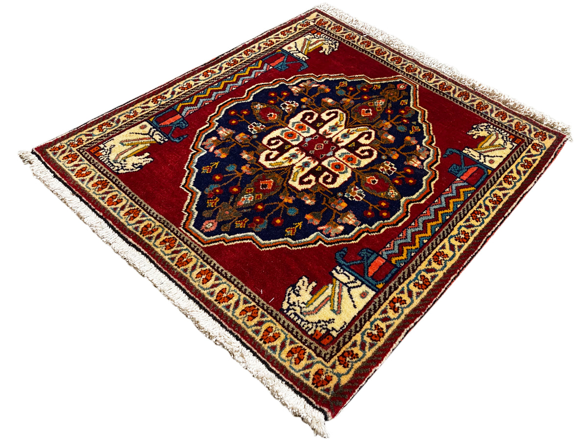 Tapete com fundo vermelho, motivo central azul-escuro, barras ornamentais bege e franjas