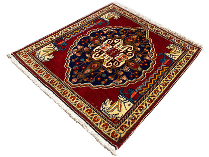 Tapete com fundo vermelho, motivo central azul-escuro, barras ornamentais bege e franjas