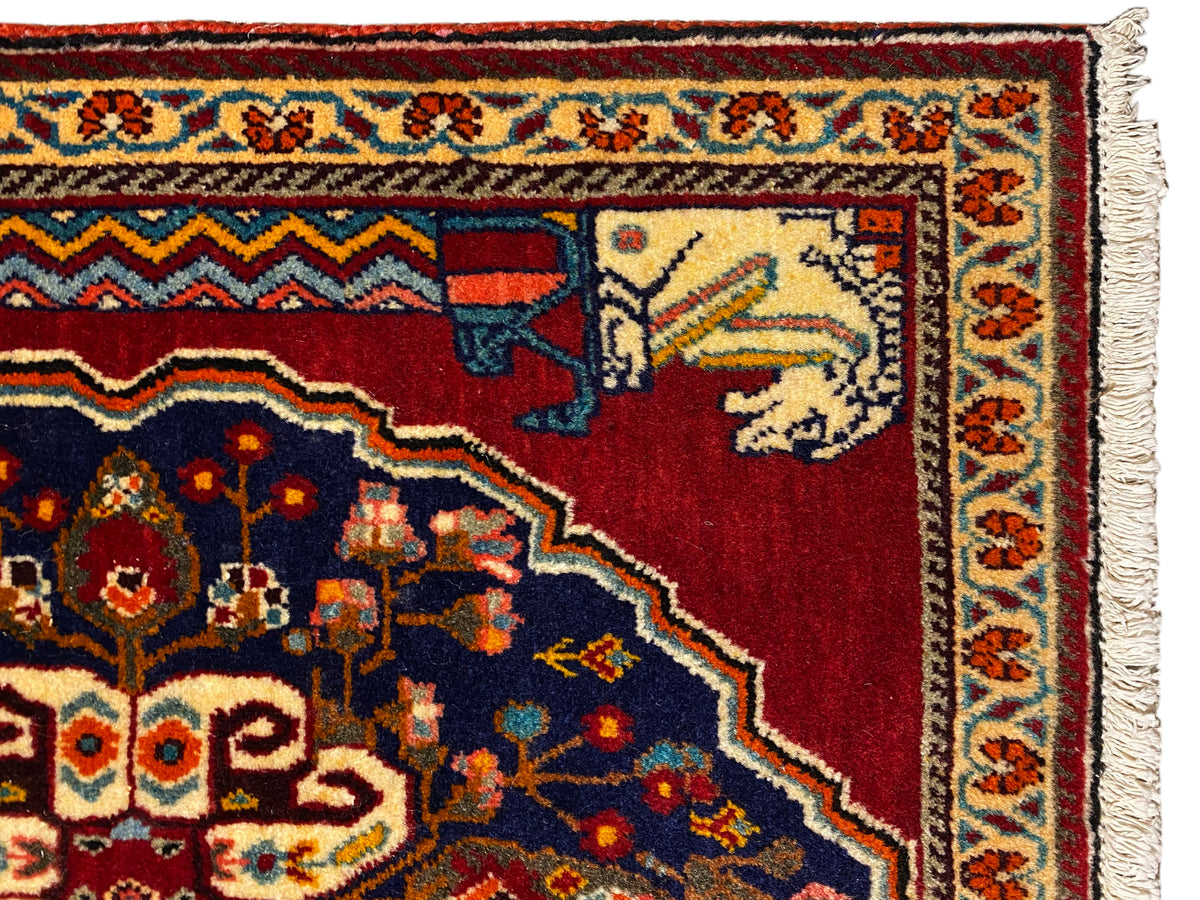 Vista detalhada: padrão de tapete vermelho e azul-escuro com elementos de animais/figuras bege