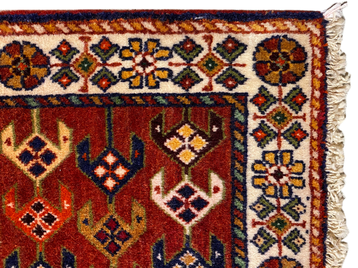 Detalhe do tapete: superfície vermelha com orla ornamentada, losangos coloridos e bordas laterais desfiadas