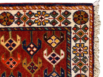 Detalhe do tapete: superfície vermelha com orla ornamentada, losangos coloridos e bordas laterais desfiadas