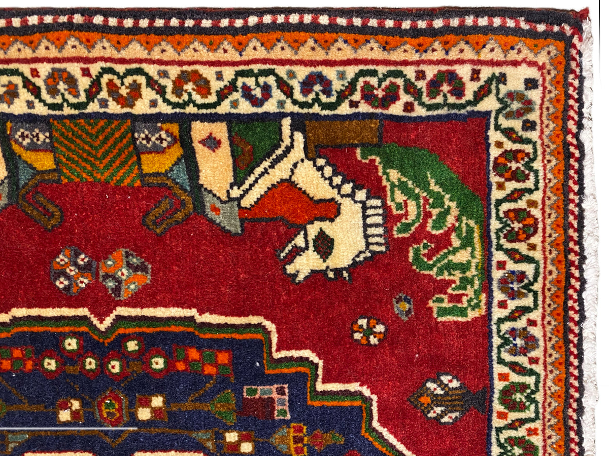 Grande plano de um tapete Poshti, campo vermelho com animais, contorno decorativo azul e bordadura com padrão