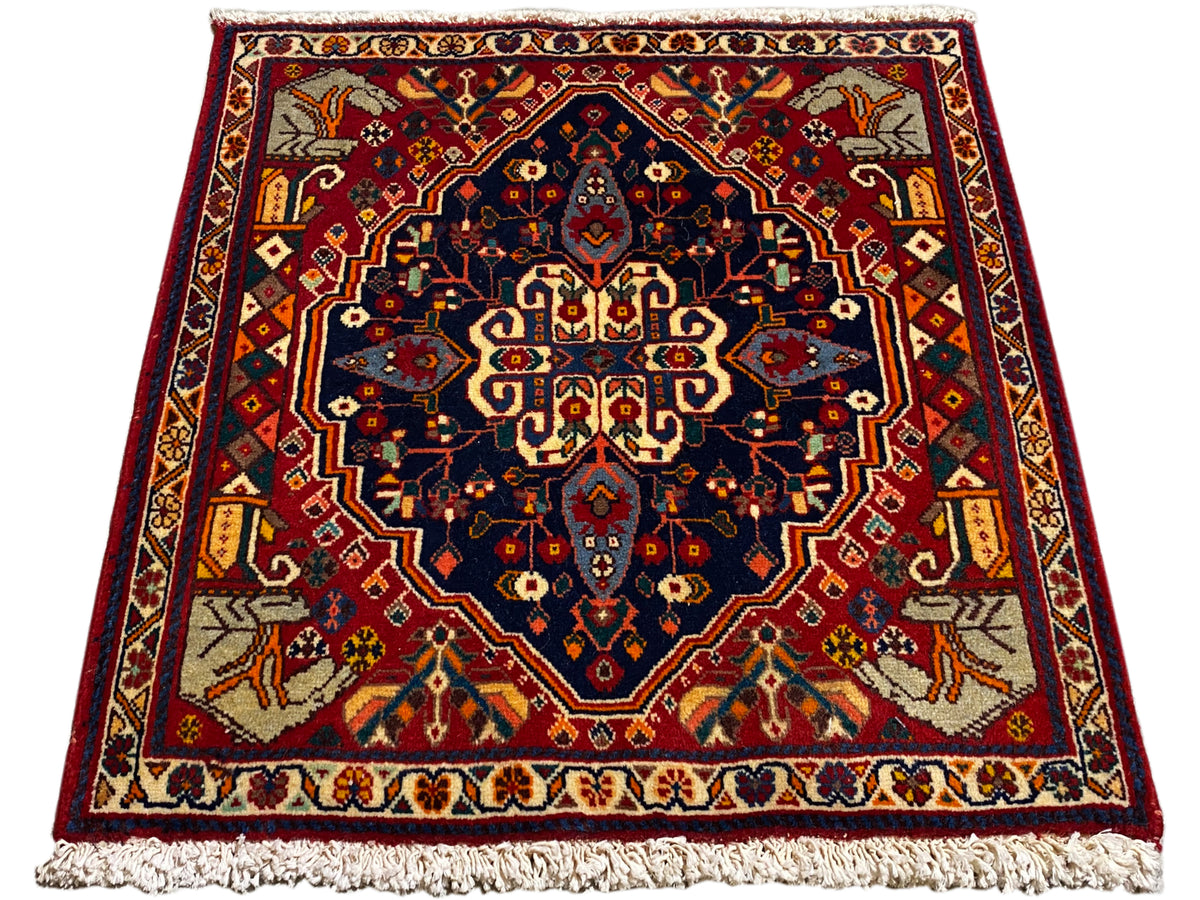 Tapete vermelho e azul-escuro com ornamento central, formato retangular e franjas