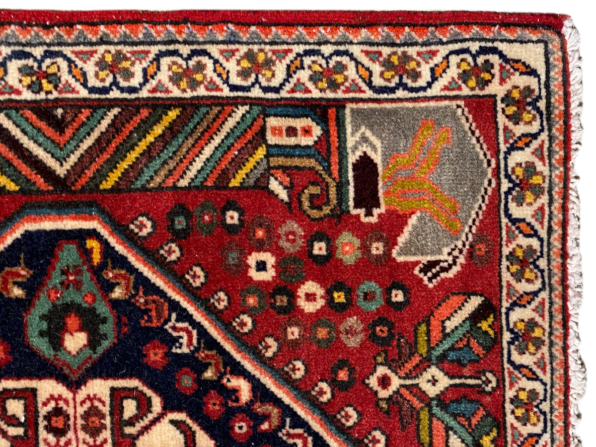 Vista detalhada: tapete vermelho com motivos ornamentais, borda multicolorida e franjas