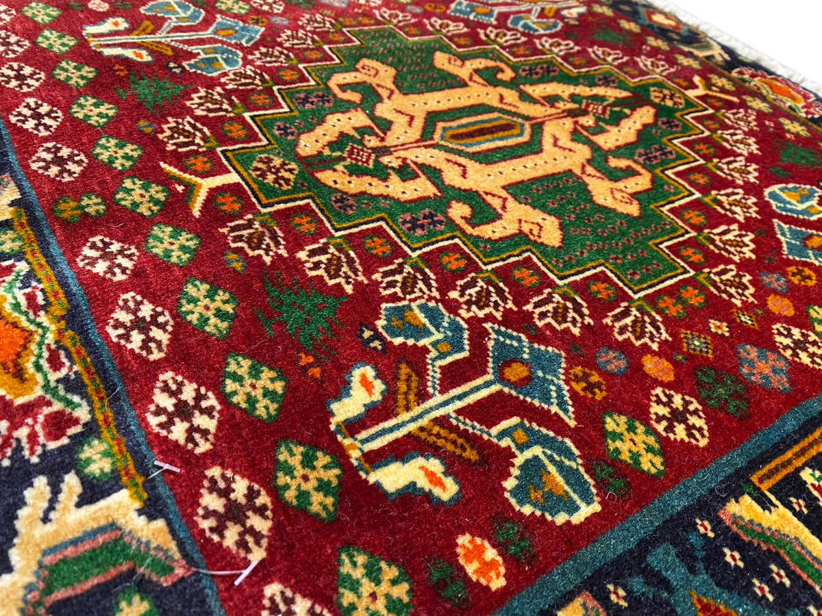 Pormenor da parte da frente de um tapete com campo vermelho, padrões em forma de estrela e linhas turquesa, pelo texturado