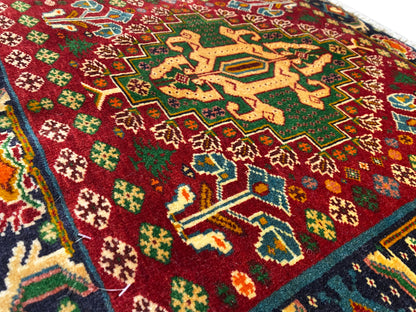 Pormenor da parte da frente de um tapete com campo vermelho, padrões em forma de estrela e linhas turquesa, pelo texturado