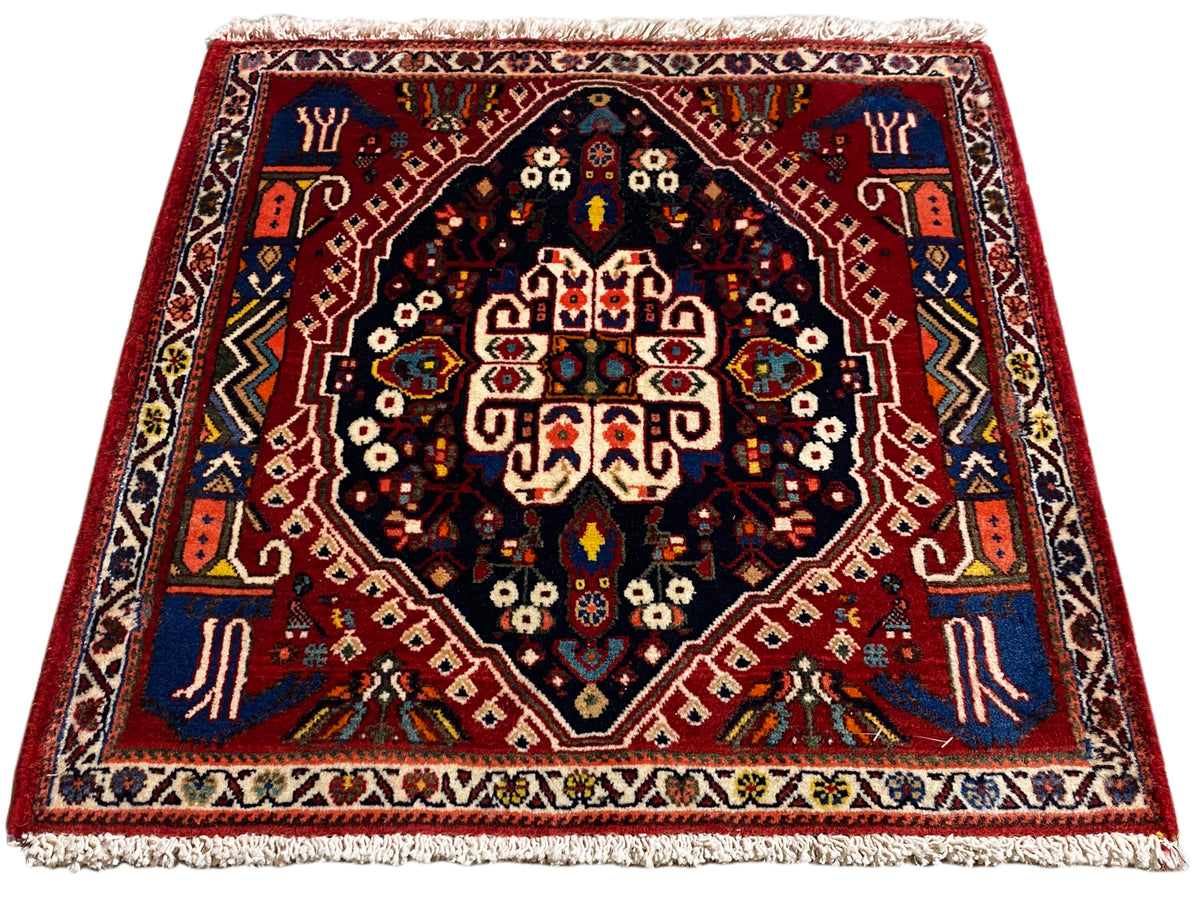 Tapete com rebordo vermelho, centro azul-escuro e ornamentos multicoloridos, franjas