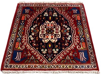 Tapete com rebordo vermelho, centro azul-escuro e ornamentos multicoloridos, franjas