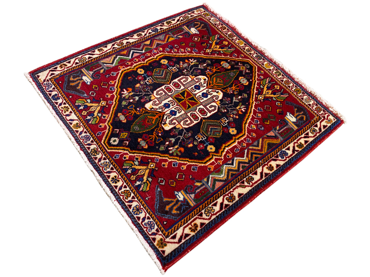 Tapete Poshti (67×67 cm) na diagonal: fundo vermelho, centro escuro com padrões brancos