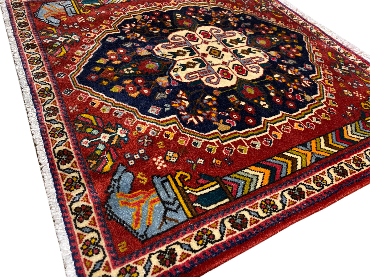 Pormenor do tapete Poshti 65x61 cm: campo vermelho, ornamento azul-preto, bordas contrastantes